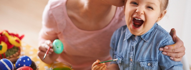 child laughing while being embraced by woman and painting eggs