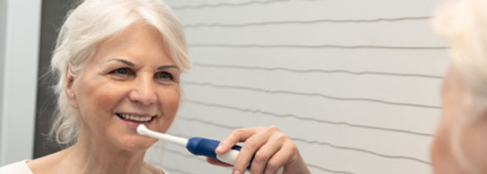 senior woman brushing her teeth in the mirror