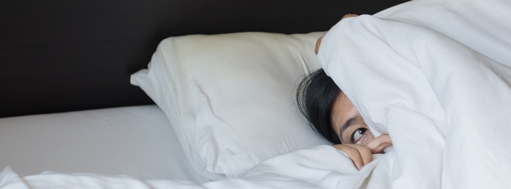 person laying in bed peeking out from under the covers