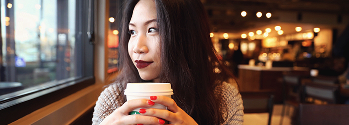 woman clutching a cup of hot coffee looking out the window