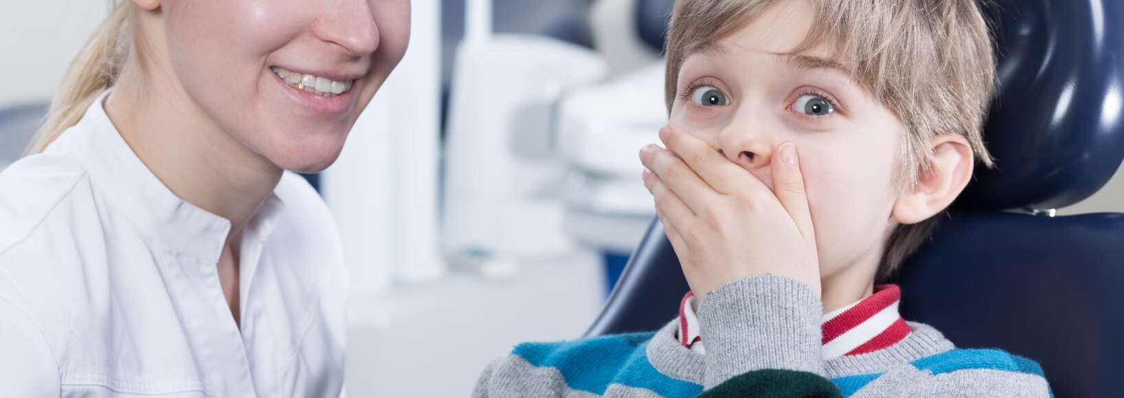 boy in dentist chair covering his mouth in fear