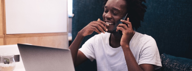 man smiling on the phone while looking at computer