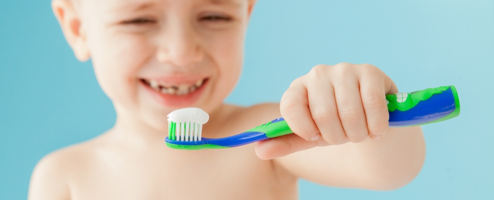 boy holding out toothbrush with toothpaste on it