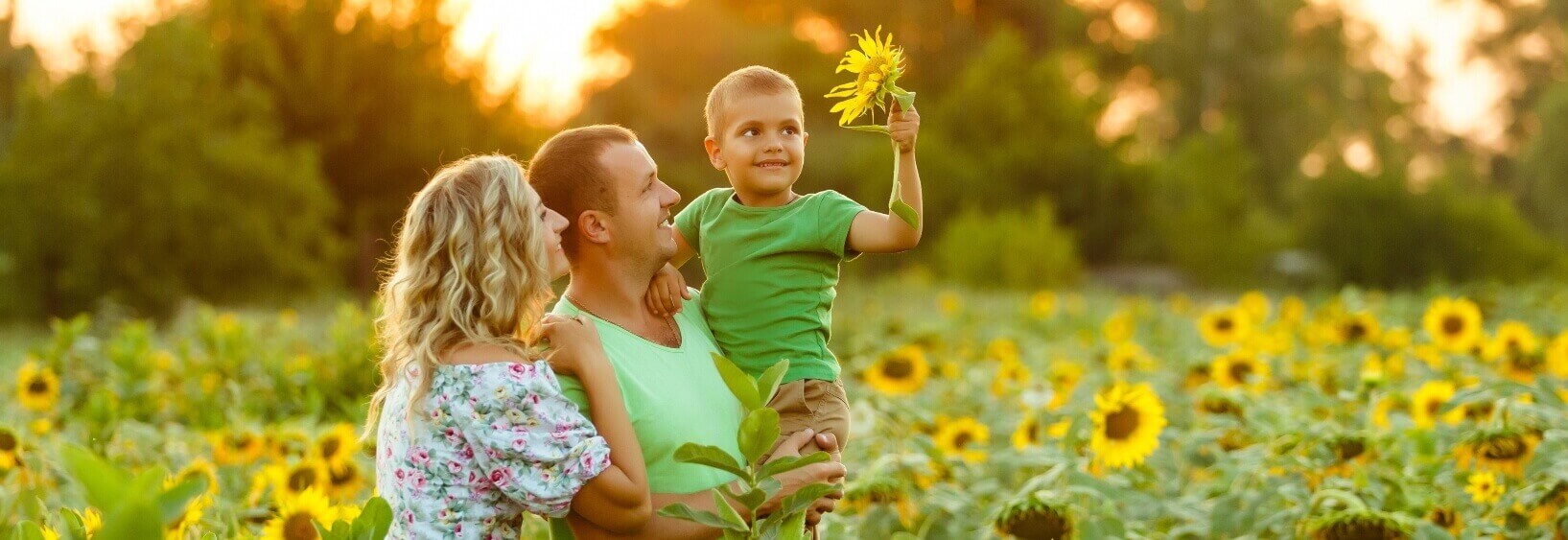 mother and father holding son and smiling in sunflower field