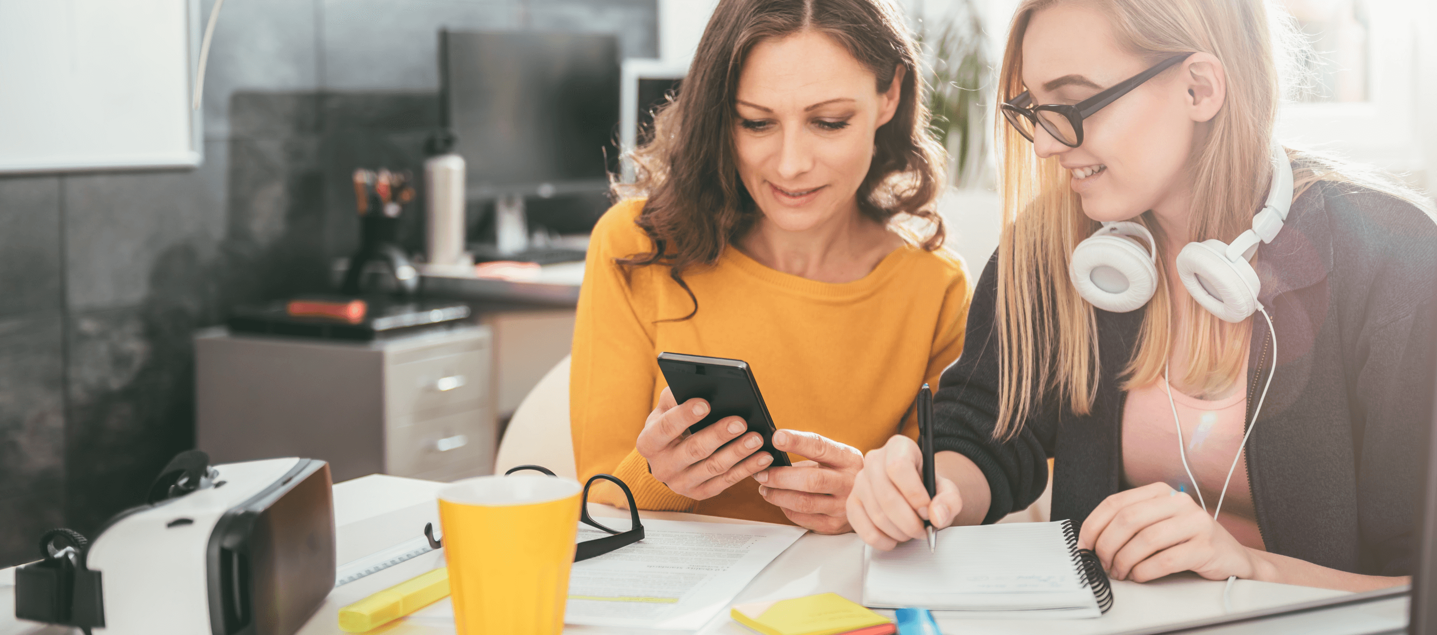 woman in yellow shirt showing woman with headphones around her neck dental insurance plans on her iphone