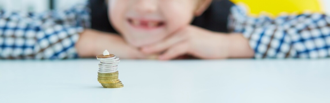 boy looking at lost tooth on top of stack of coins